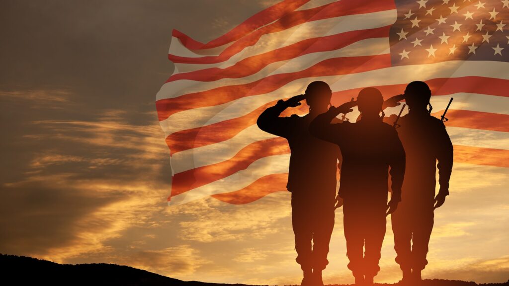 Soldiers saluting in front of an American flag at sunset